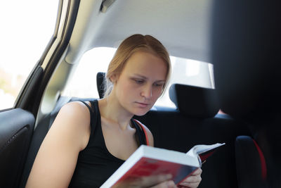 Young woman reading book in car