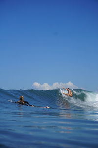 People swimming in sea against clear blue sky