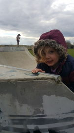 Portrait of cute girl standing by sports ramp against cloudy sky at park