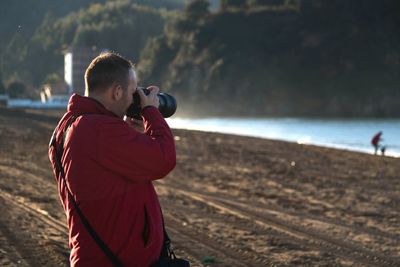 Side view of man photographing with digital camera at beach