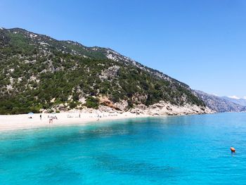 Scenic view of mountains by sea against blue sky at sardinia