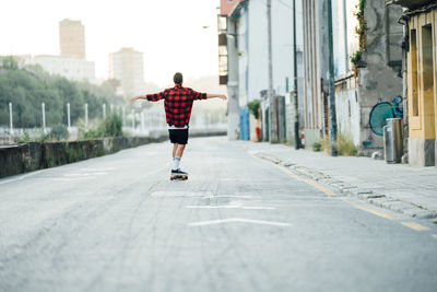 Full length rear view of man skateboarding on city street