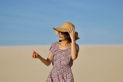 Woman in hat standing at beach against sky