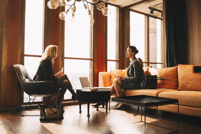 Full length of female lawyers discussing while sitting by window at office