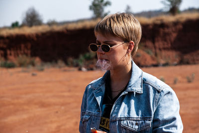 Young woman wearing sunglasses smoking while standing outdoors