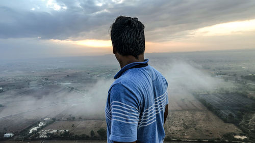 Rear view of man standing on landscape against sunset sky