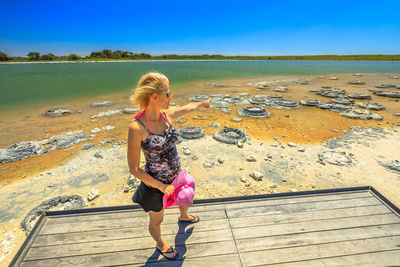 Full length of woman pointing while standing on shore against sky