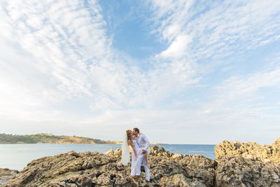 Woman standing on rock by sea against sky