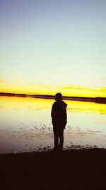 Rear view of silhouette man at beach against sky during sunset