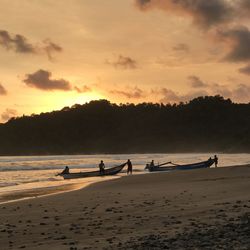 Silhouette people on beach against sky during sunset