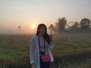 Woman standing on field against sky during sunset