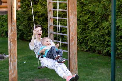 Cheerful mother and son swinging in park