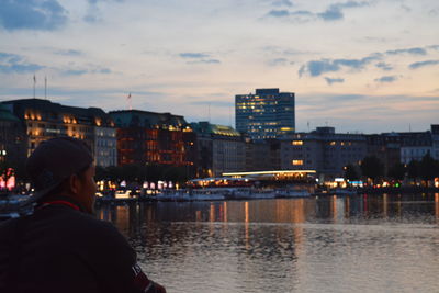 Rear view of man looking at river by buildings against sky