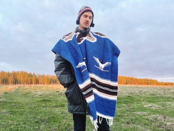 Portrait of young woman standing on field against sky