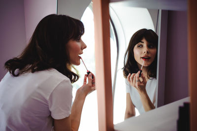 Close-up of young woman applying red lipstick in front of mirror at home