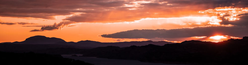 Scenic view of silhouette mountains against dramatic sky during sunset