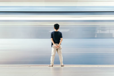 Rear view of boy standing by moving train at railroad station platform