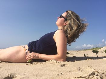 Woman lying at beach against sky