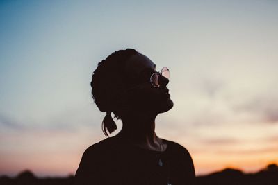 Woman wearing sunglasses against sky during sunset