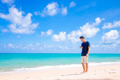 Young man using phone while standing on sand at beach