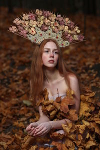 Thoughtful young woman wearing flowers on hair sitting at forest during autumn