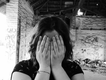 Close-up of woman covering face with hands at abandoned house