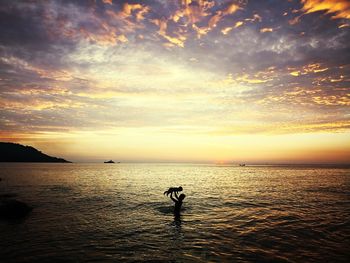 Silhouette man standing in sea against sky during sunset