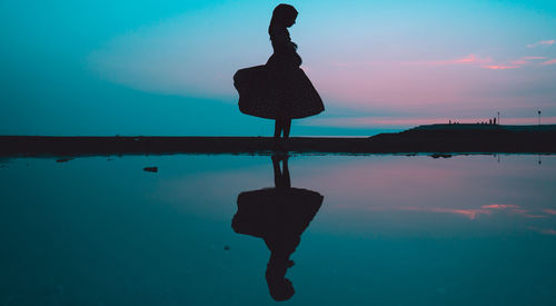 Silhouette woman at beach against sky at night