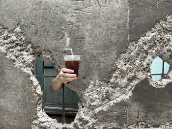 Hand holding iced coffee from the break gap of old wall. summer drink concept.