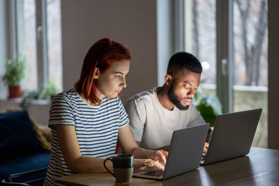 Focused entrepreneurs caucasian woman african american man work on laptops in home office together.