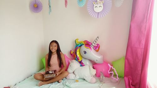 Full length portrait of smiling girl holding cake while sitting by toys at home