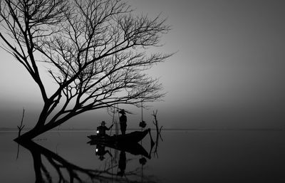 Silhouette bare tree by lake against clear sky