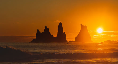 Silhouette rock formation in sea against orange sky