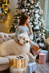 Little cute girl sitting on the sofa with samoyed dog