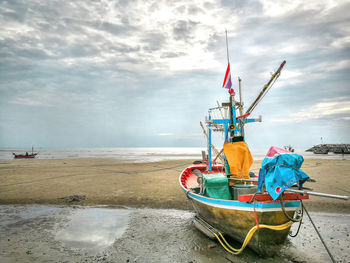 Fishing boat moored at beach against cloudy sky