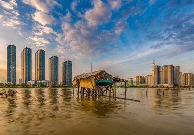 Buildings at waterfront against cloudy sky