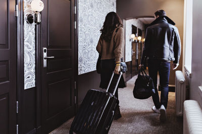 Rear view of couple walking with luggage in corridor of hotel room