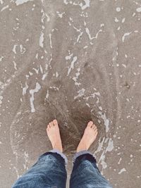 Low section of person standing on wet sand