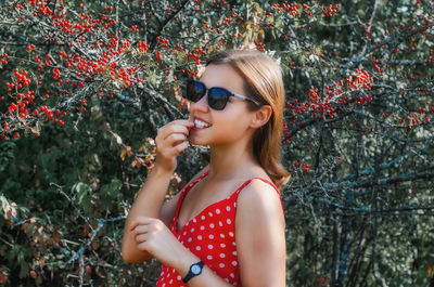 Young woman in red dress eats red berries from hawthorn bush