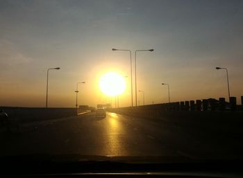 Silhouette road by sea against sky during sunset