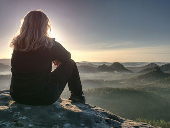 Blond woman sitting on the edge of the mountain cliff against beautiful mountains peak. travel style