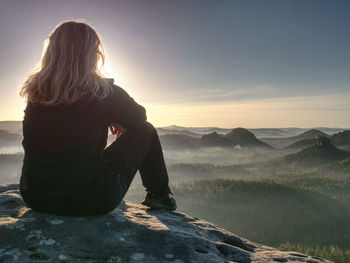 Blond woman sitting on the edge of the mountain cliff against beautiful mountains peak. travel life