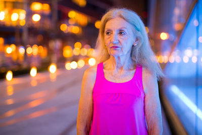 Portrait of woman standing against illuminated city at night