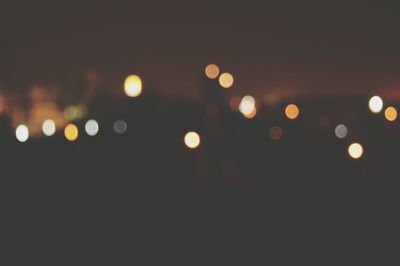 Defocused image of illuminated lights against sky at night