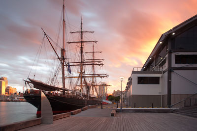 Sailboats moored at harbor against sky during sunset