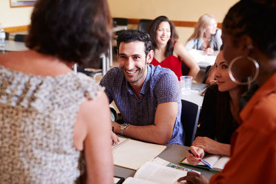 Happy male student looking at teacher while sitting with friends in language school