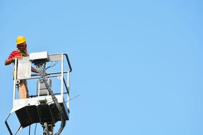 Low angle view of technician standing on hydraulic platform against clear sky