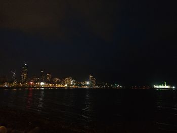 Illuminated buildings by sea against sky at night