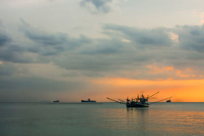 Fishing boat on sea against cloudy sky during sunset