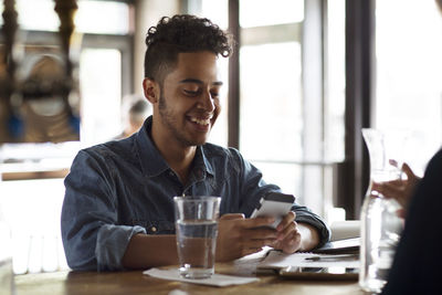 Smiling young man using phone at bar counter in cafe